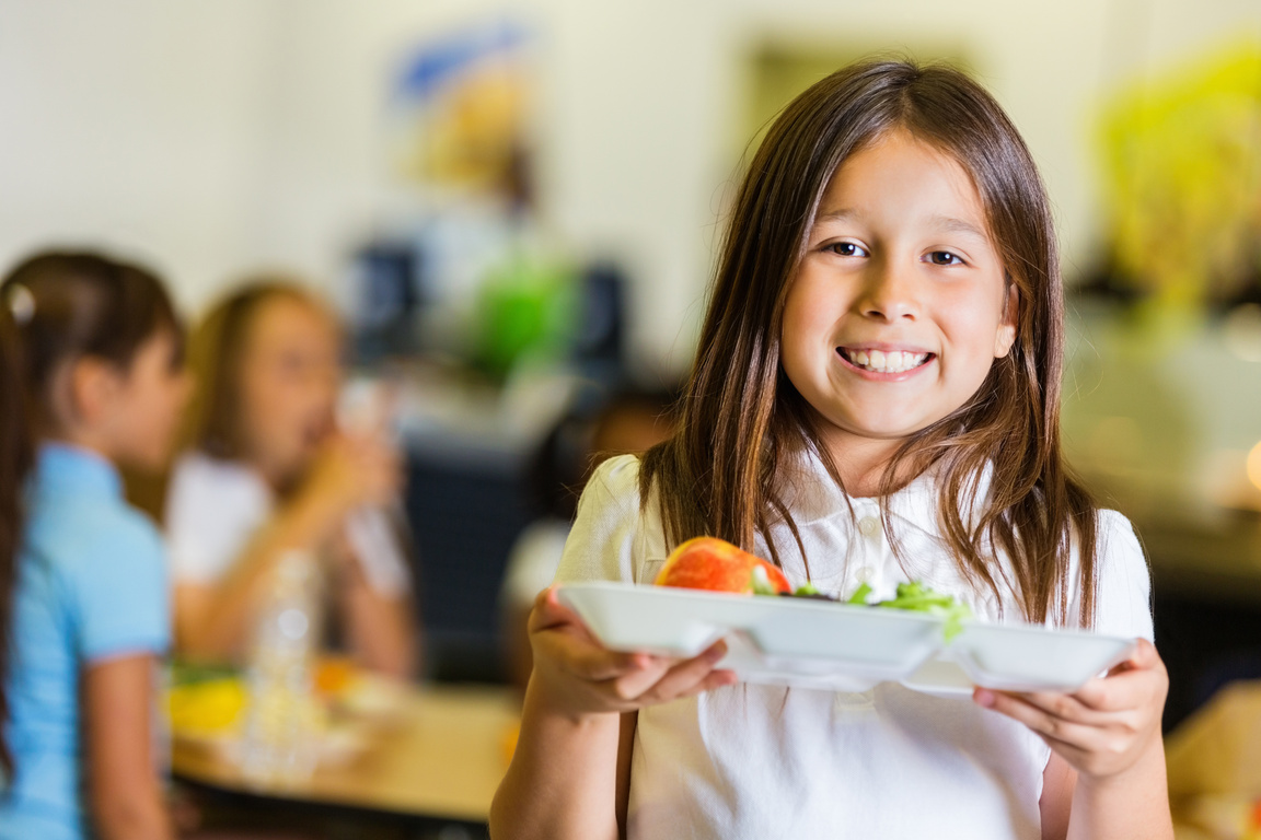 Cute elementary student holding lunch tray in school cafeteria